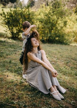 Delikanlı şakacı bir şekilde annesinin dışarıda kıvırcık saçlarını yapıyor. 