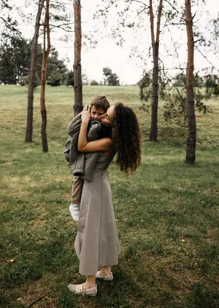 Annem bulutlu bir günde yeşil bir parkta gülümseyen oğlunu öper..