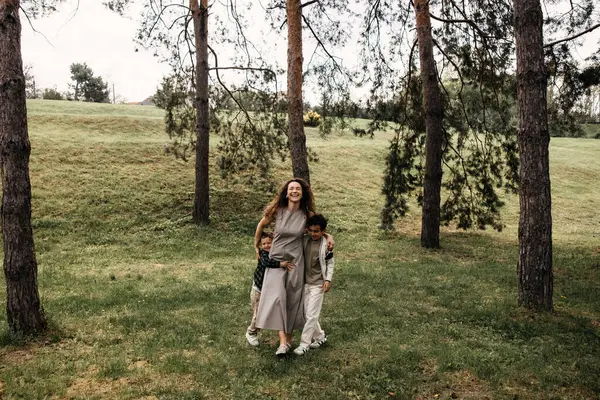 Mutlu anne iki oğluyla güneşli bir orman çayırında yürüyor..