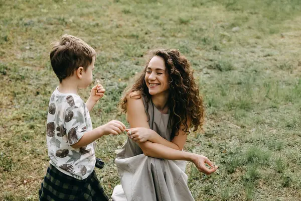 Gülümseyen anne ve oğul dışarıda karahindiba ile oynuyorlar..