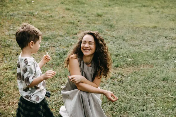 Gülümseyen anne ve oğul dışarıda karahindiba ile oynuyorlar..