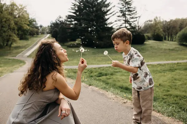 Anne ve çocuk bahar parkında karahindiba üflüyor.
