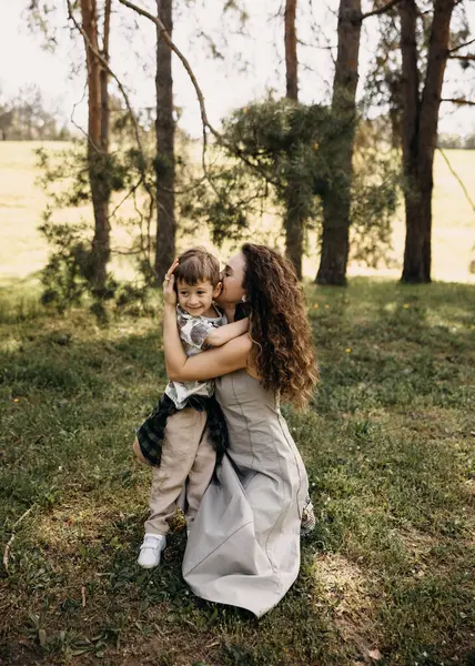 Mutlu anne ormanda gülümseyen oğlunu öpüp kucaklıyor.