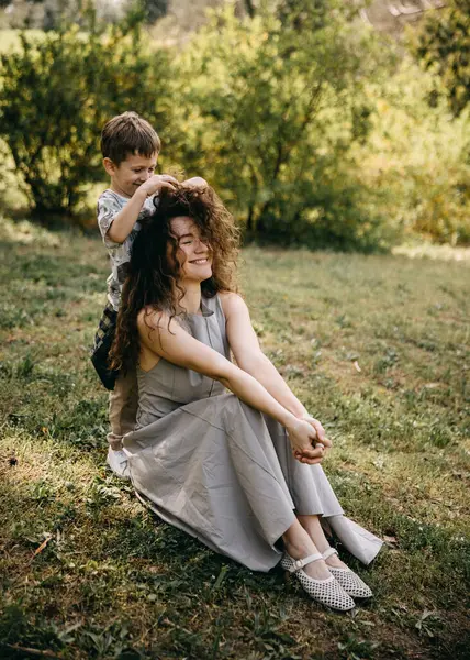 Delikanlı şakacı bir şekilde annesinin dışarıda kıvırcık saçlarını yapıyor. 