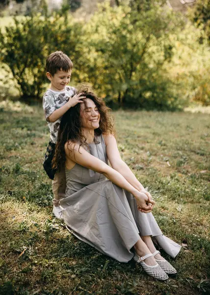 Delikanlı şakacı bir şekilde annesinin dışarıda kıvırcık saçlarını yapıyor. 
