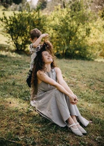 Delikanlı şakacı bir şekilde annesinin dışarıda kıvırcık saçlarını yapıyor. 