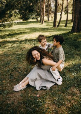 Neşeli anne, güneşli bir ormanda iki oğluyla oynayıp gülüyor..
