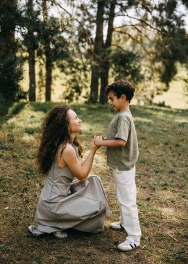 Anne ve oğlunun bir orman parkında hassas bir anda el ele tutuşmalarının yakın çekimi. Duygusal aile bağlantısı.