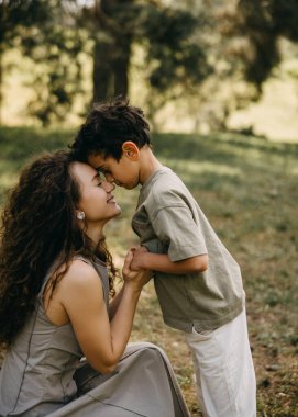 Anne ve oğlunun alınlarını birbirine bastırdığı ve bir orman parkında gülümsediği yakın çekim. Duygusal aile bağlantısı.