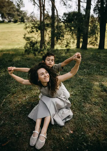 Bir anne ve oğlunun çimenlerde birlikte oynadığı mutlu bir an. Ormandaki uçak kanatları gibi kollarını çırpıyorlar..