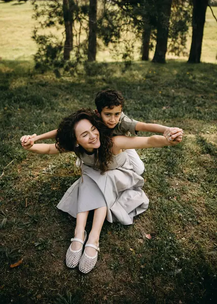 Bir anne ve oğlunun çimenlerde birlikte oynadığı mutlu bir an. Ormandaki uçak kanatları gibi kollarını çırpıyorlar..