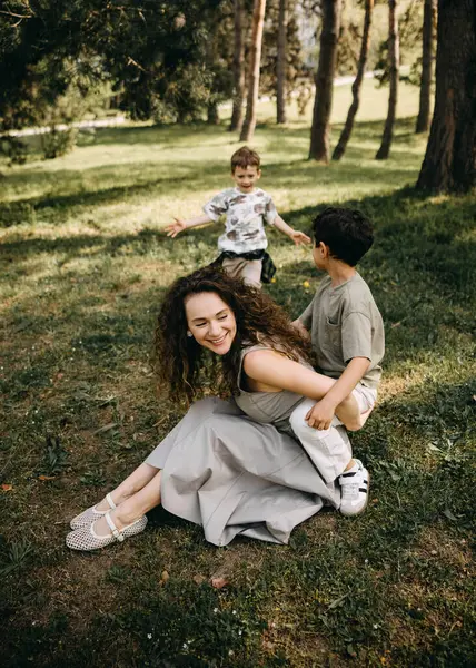 Neşeli anne, güneşli bir ormanda iki oğluyla oynayıp gülüyor..