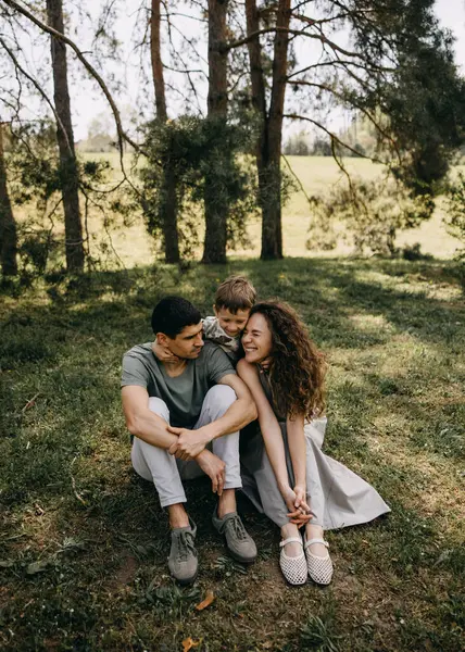 Aileler ormanda birlikte güzel vakit geçiriyorlar, çimenlerin üzerinde oturup, gülümsüyorlar ve çocuklarına sarılıyorlar..