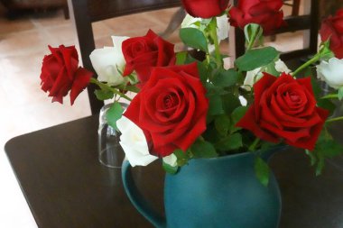 Masanın dekorasyonu için mavi seramik vazoda bir buket kırmızı gül.