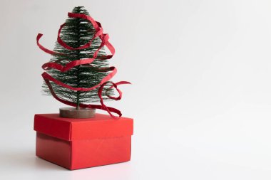 Kırmızı kağıt kurdeleyle sarılı kırmızı hediye kutusuna yerleştirilmiş küçük Noel Ağacı ,