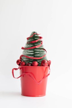 Kırmızı teneke kutuya yerleştirilmiş küçük Noel Ağacı. Kırmızı karton kurdeleyle sarılı kırmızı Noel Baloları asılmış. ,