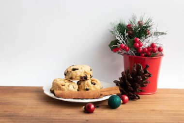 Beyaz seramik tabakta çörek, kahverengi kozalak, kırmızı böğürtlenli kırmızı teneke kutu, yeşil köknar