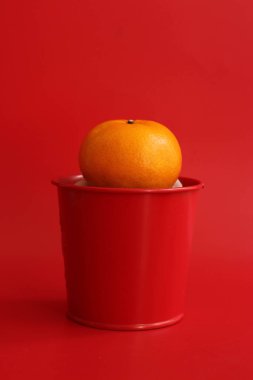 An Orange in a red tine can on Red Background