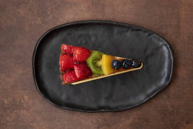 Beyaz arka planda lezzetli Danimarka meyveli keki, üstüne taze çilek, kivi, şeftali ve yaban mersini.