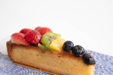 Beyaz arka planda lezzetli Danimarka meyveli keki, üstüne taze çilek, kivi, şeftali ve yaban mersini.