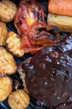 Izgara sebzeli domuz pirzolası, domates, havuç ve patates, beyaz arka planda.