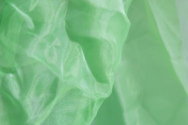 Yeşil organza kumaşının dalgalı dokusu ve gri arka planda soyut kırışıklıklar.