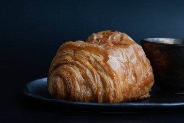 Siyah arka planda bir fincan kahveli çikolatalı kruvasan.