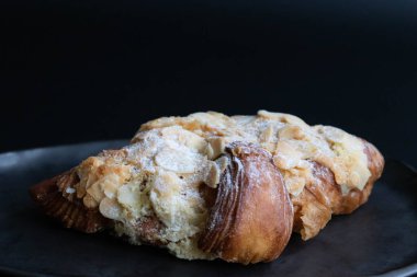 Siyah arkaplanda bir parça badem kruvasanı.