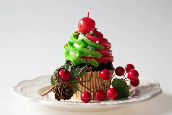 Christmas Chocolate Cup Cake with red and Green cream topped with Red Cherry on White Background, decorated with Green Fir and Red Berries