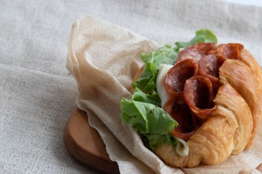 Salamlı sandviç, marul ve peynirli, siyah arka planda.