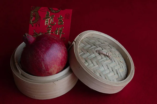 Red pomegranate on a Dim-Sum Basket with Red Lucky Envelope with Chinese Script for Good Luck on red background