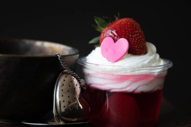 Beyaz kremalı çilek reçeli ve pembe kalpli taze çilek, siyah arkaplan.