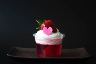 Beyaz kremalı çilek reçeli ve pembe kalpli taze çilek, siyah arkaplan.