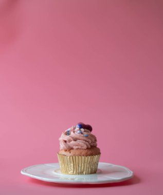 Üstünde pembe krema ve pembe arkaplanda kırmızı kalp olan vanilyalı kek.