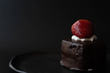 Üzerinde siyah arka planda taze çilek olan çikolatalı pasta.