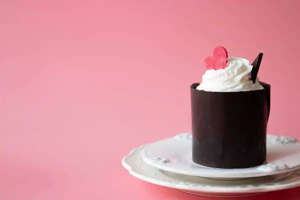 Chocolate Mousse cake topped with White Whipped Cream and Red Heart on Pink background