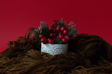 Sıcak Noel, kırmızı arka planda kahverengi yün örgü ile sarılmış beyaz seramik bardakta kırmızı böğürtlen