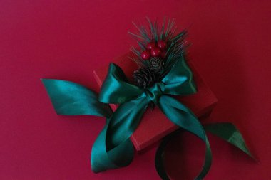 Red Gift Box with Green ribbon and a bouquet of Red Berries on Red Background clipart