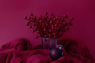 a bouquet of red berries in a glass on red background with a red hanging ball , red background clipart