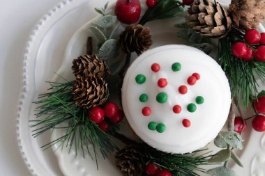 Kırmızı ve yeşil Noel süslemesi ile kaplı, kırmızı böğürtlen ve yeşil köknar ile çevrili, beyaz arka plan