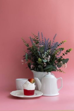 Hoş bir öğleden sonra çay saati, krem şantili kırmızı jöle, beyaz çay fincanı ve çay demliği. Pembe Arkaplan