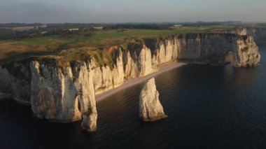 Etretat 'ın baş döndürücü uçurumlarını gün batımının sıcacık ışığında güneşlenirken tecrübe edin. Altın renkler sakin sulardan yansıyarak ruhu büyüleyen büyüleyici bir manzara yaratır..