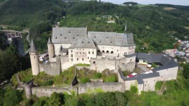 Vianden Kalesi 'nin nefes kesici mimarisini keşfedin. Açık mavi gökyüzü altında canlı yeşillikler ve resim gibi manzaralarla çevrili..