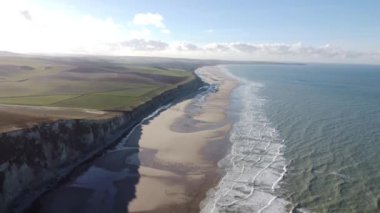 Cap Blanc-Nez 'in dingin güzelliğini deneyimleyin. Dalgalar, dingin bir sabah gökyüzü altında yemyeşil kayalıkların çerçevelediği altın kumlara ritmik olarak çarpar..