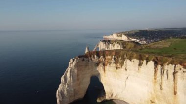 Güneş ışığı ikonik beyaz uçurumlarda dans ederken ve dalgalar yavaşça kıyıya vururken Etretat 'ın nefes kesici manzarasını deneyimleyin. Huzurlu bir kıyı ortamında doğa güzelliği sergileniyor..