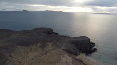 Güneş dramatik sahil şeridinde batarken Lanzarote 'nin dingin güzelliğini hissedin. Sakin sular alacakaranlığın canlı renklerini yansıtıyor ve büyülü bir atmosfer yaratıyor..
