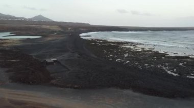 Güneş, Lanzarote 'nin volkanik manzaralarının üzerinde batarken sakin bir an yaşayın. Siyah kumlu plajlar, bu sakin ortamda çarpan dalgalarla karşılaşıyor, doğal güzellikleri sergiliyor..
