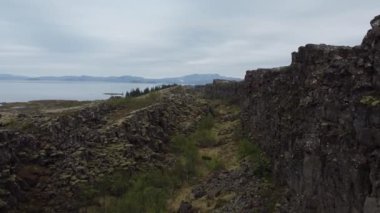 Thingvellir 'in çarpıcı jeolojik oluşumlarını keşfedin. Yeşillik, sakin bir göl kenarında kayalık kayalıklarla buluşur ve doğal güzelliklerle dolu sakin bir atmosfer yaratır..