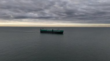 Muazzam bir kargo gemisi, engin bir su kütlesiyle çevrili sakin denizde sorunsuzca süzülüyor. Akşam gökyüzünde gri bulutlardan oluşan bir duvar halısı var. Alacakaranlıkların gelişini işaret ediyor..