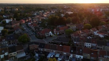 Güneş batarken, Belçika 'nın pitoresk bir banliyösü büyüleyici evleri ve sessiz caddeleriyle açılıyor. Sıcak ışık bölgeyi yıkıyor, sakin akşam atmosferini sergiliyor..
